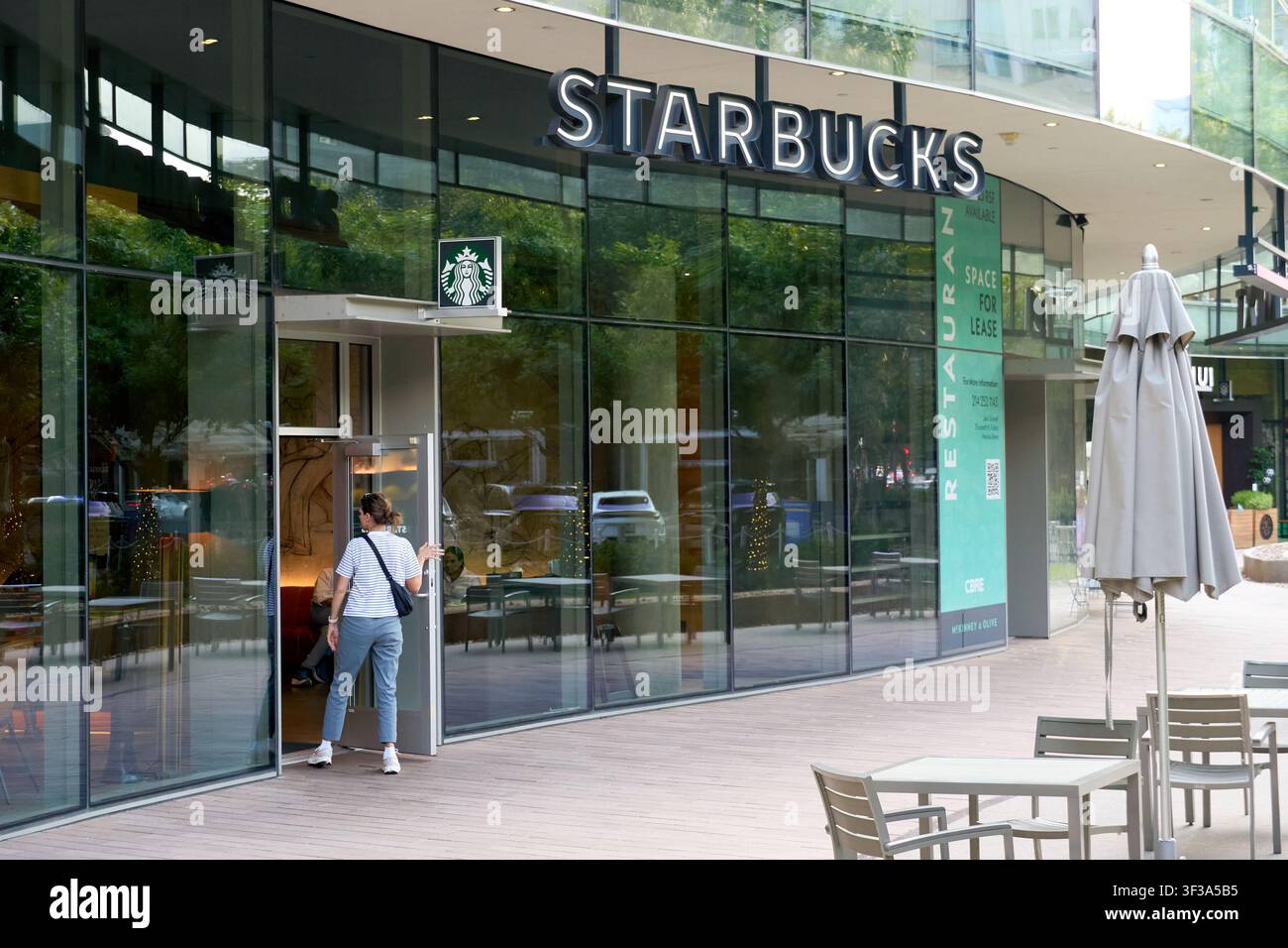 DALLAS, TX, USA - 13 LUGLIO 2026: Un cliente entra in un negozio Starbucks, con facciata in vetro e una segnaletica ben visibile. Starbucks è un marchio globale di caffetterie Foto Stock