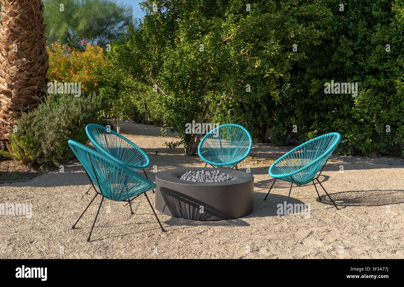 Sedie da giardino color turchese e focolare in un cortile di paesaggio desertico durante il giorno. Disposizione di sedute circondata da una vegetazione rigogliosa e in una giornata soleggiata. Foto Stock