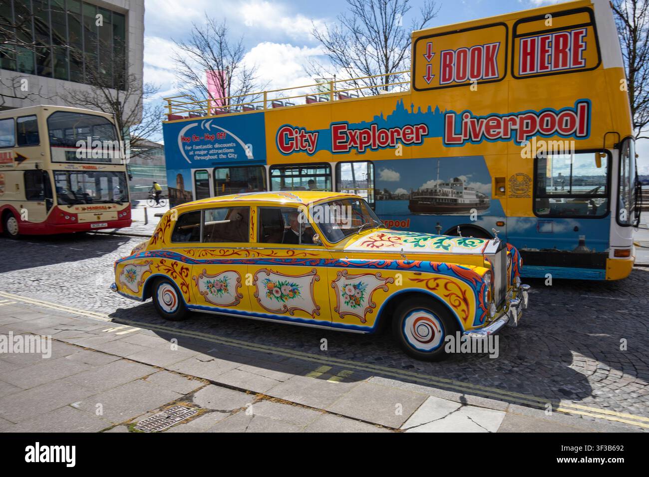 Una replica della famosa Rolls-Royce Phantom V psichedelica di John Lennon parcheggiata accanto a un autobus turistico giallo City Explorer di Liverpool al Pier Head. Foto Stock