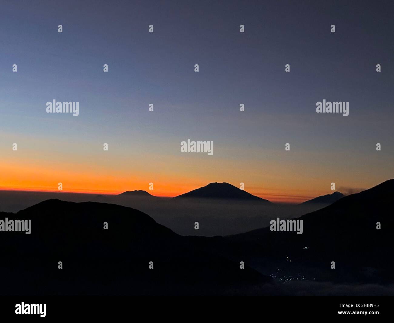 Paesaggio sereno dell'alba che mostra silouetti di montagne e vulcani a strati contro un cielo con sfumatura che passa dal blu profondo all'arancione. Foto Stock