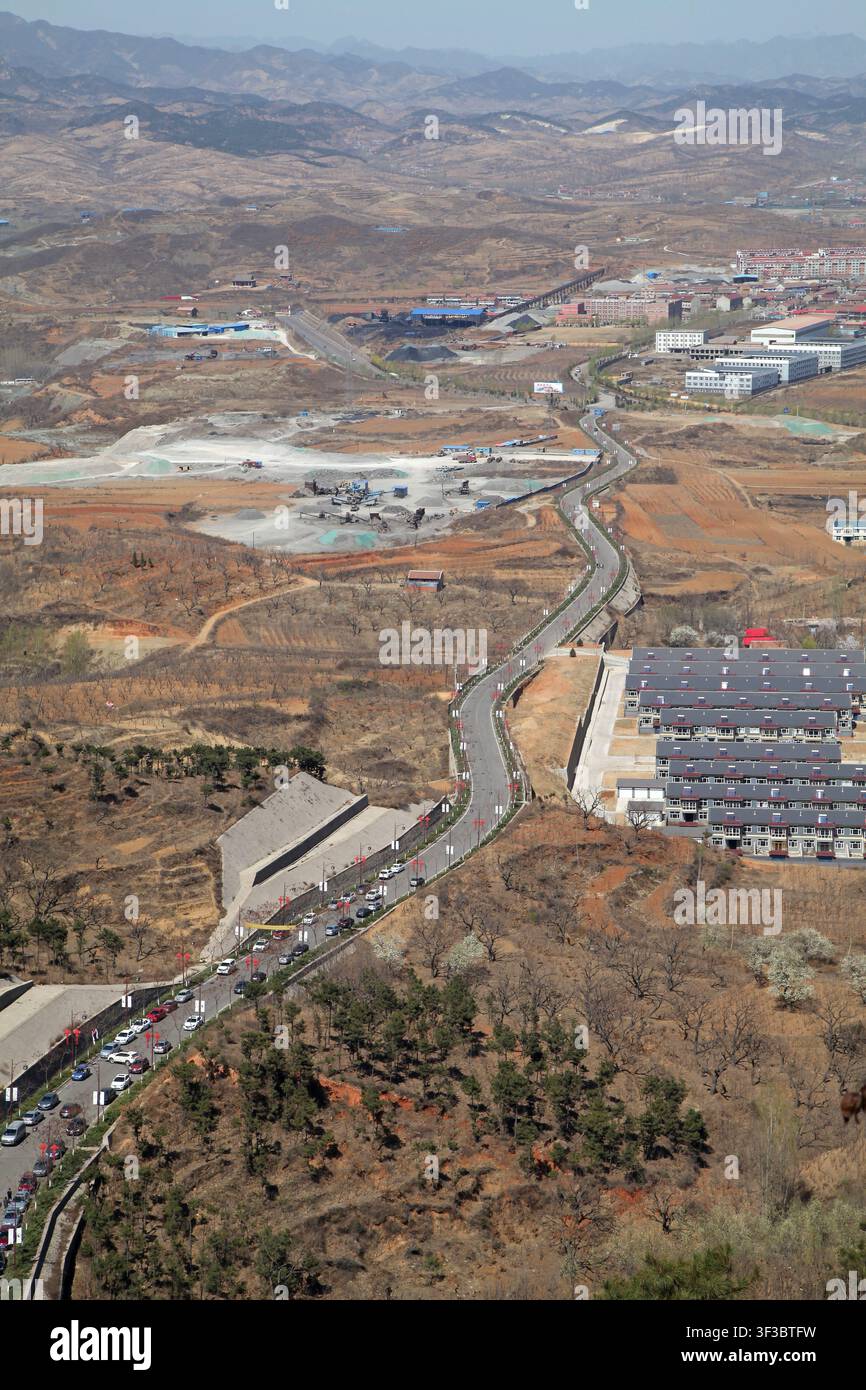 Fotografia aerea ad angolo alto che cattura una strada asfaltata sinuosa che attraversa un paesaggio rurale semi-arido. La scena presenta colline brune sterili, spar Foto Stock