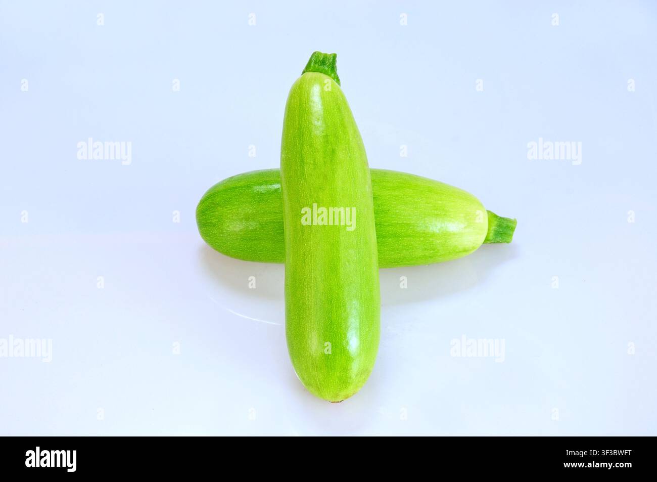 Su uno sfondo grigio chiaro, due zucchine verdi lisce e colorate sono posizionate incrociate, mostrando la loro texture fresca naturale e plu Foto Stock