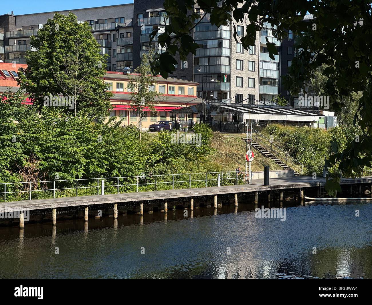 Scena urbana sul lungofiume a Uppsala, Svezia, con edifici, alberi e marciapiede pedonale lungo il fiume. - Immagine stock catturata con smartphone