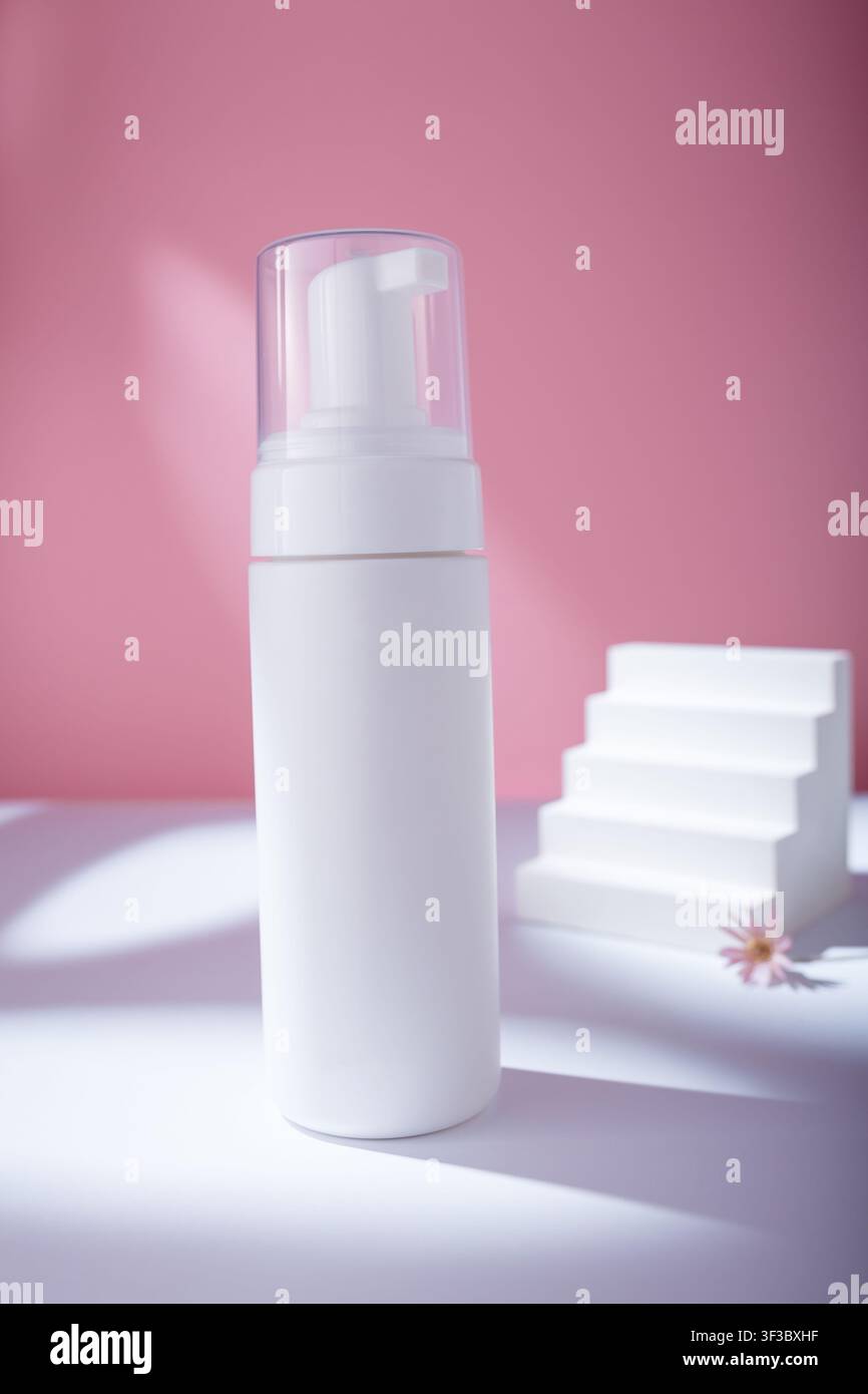 Mockup di distributore bianco su sfondo rosa in luce dura, senza template del marchio. Contenitore di schiuma detergente per il viso con fiore e scalini in cemento Foto Stock
