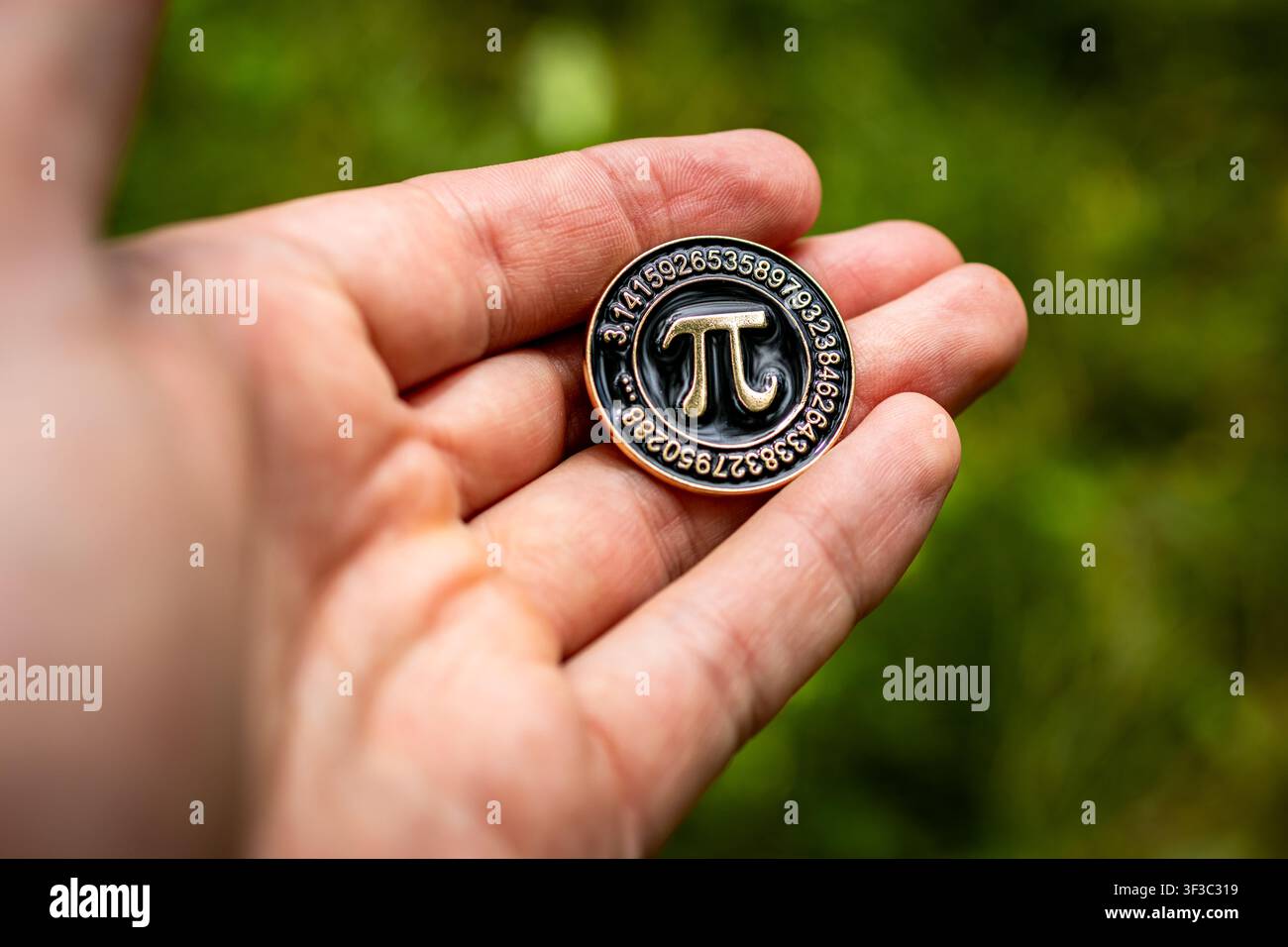 Mano tiene un anello con emblema pi rotondo cerchiato di cifre all'aperto con sfondo verde morbido che rappresenta l'entusiasmo per la matematica, la motivazione allo studio e l'orgoglio accademico i Foto Stock
