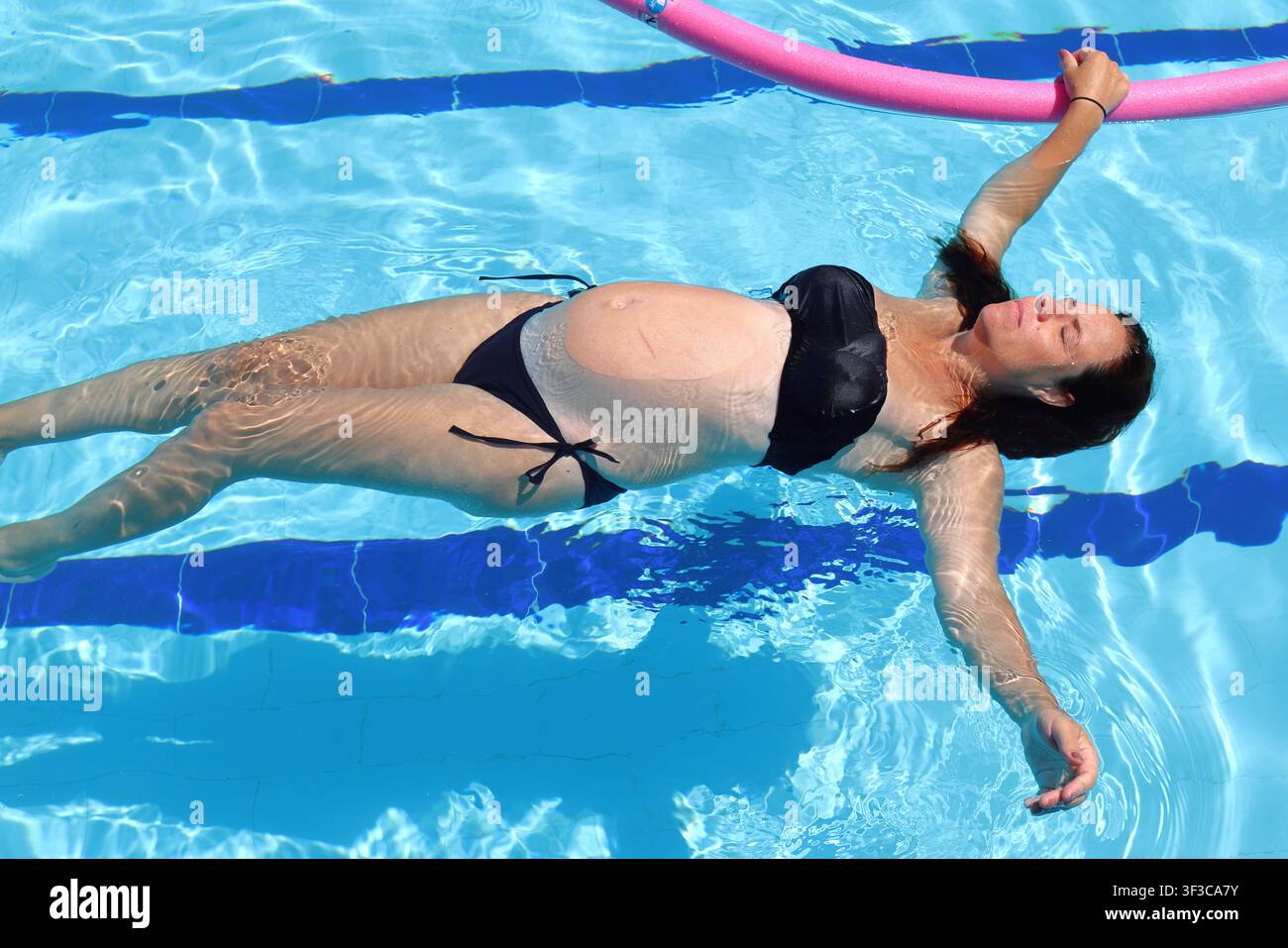Madre in attesa che si gode esercizi acquatici prenatali in una piscina Foto Stock
