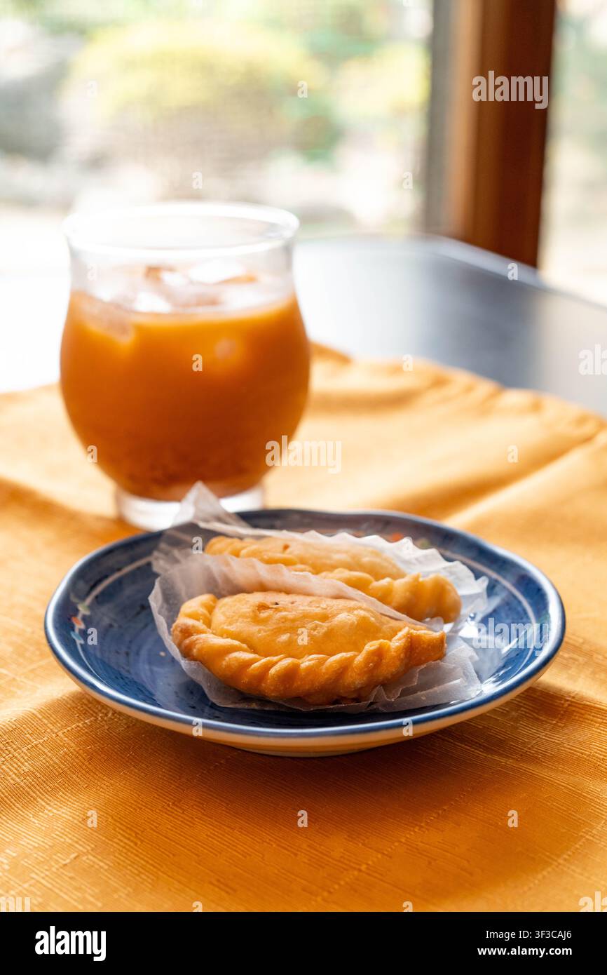 Puff di curry thailandese tradizionali serviti con tè al latte thailandese freddo in un accogliente caffè Foto Stock