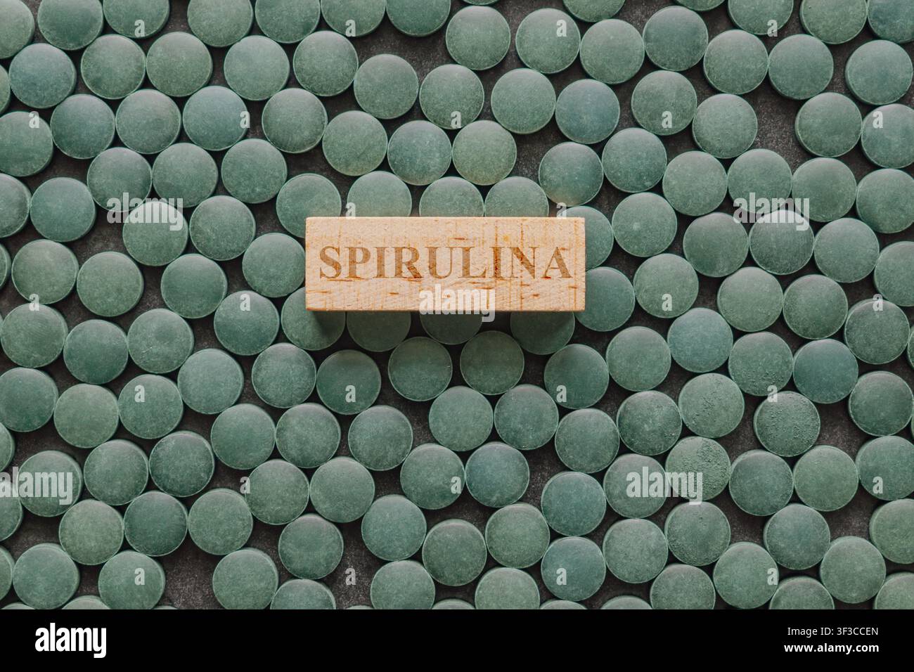 Vista piatta modello piatto composto da uno sfondo di compresse di clorella verde con etichetta in blocco di legno al centro per uno stile di vita sano dieta superfood Foto Stock