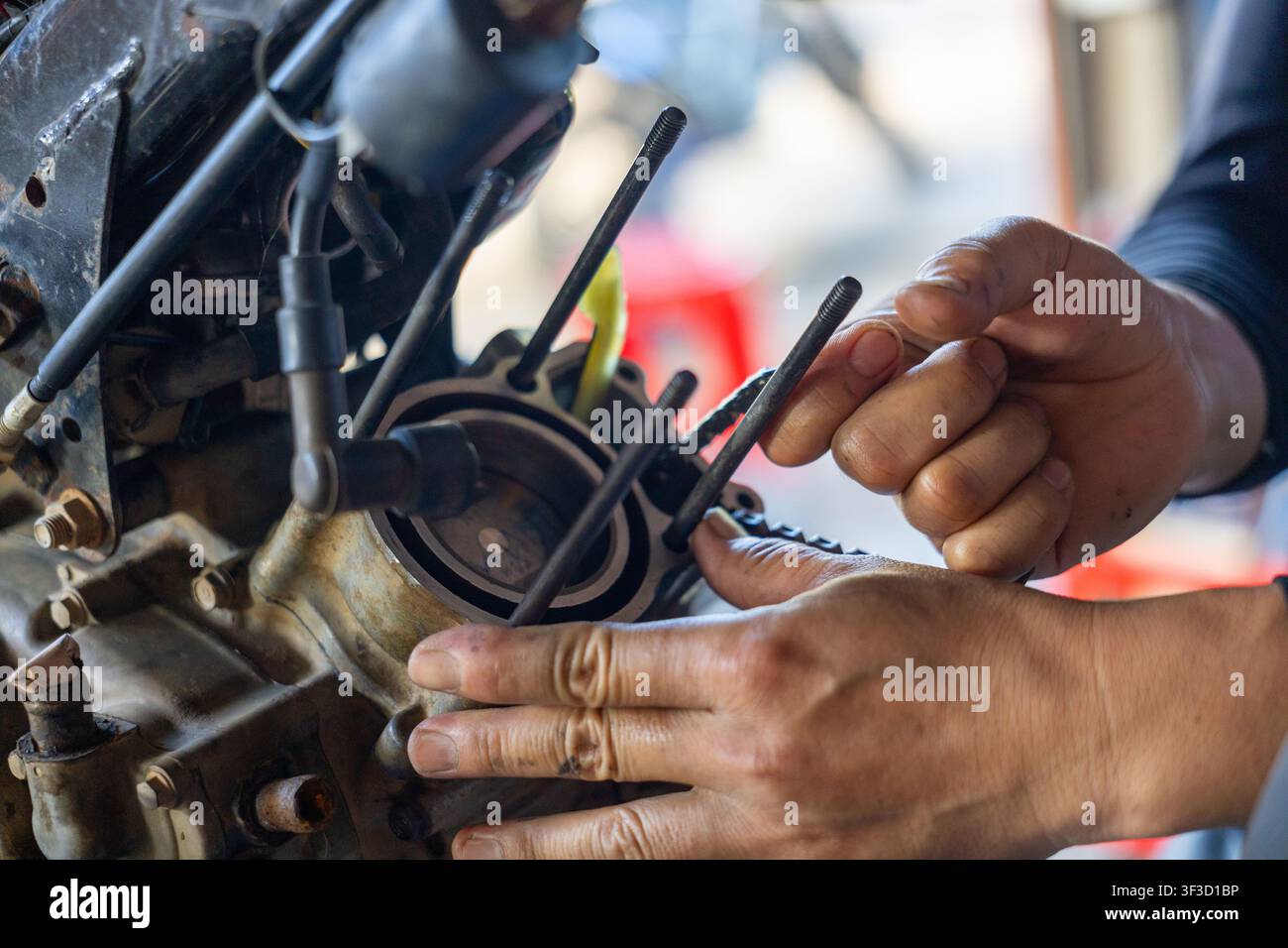 Un meccanico assembla la testata del cilindro di un piccolo motore, mostrando pistone, dadi, guarnizione e parti metalliche usurate con lavoro di riparazione concentrato e attenta manualità Foto Stock