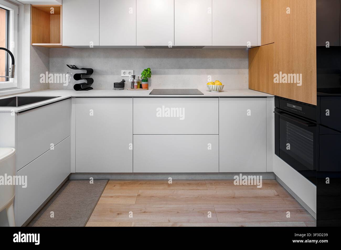 Interno di cucina minimalista moderno con armadi bianchi e accenti di legno Foto Stock