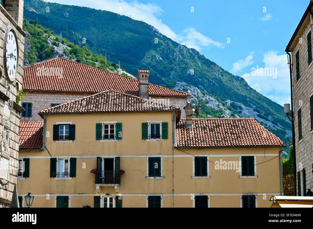 Vista panoramica di un paesaggio scenografico con case mediterranee tradizionali dai tetti di tegole rosse terracotte, facciata gialla e persiane verdi, incastonate tra montagne verdi rigogliose sotto un cielo blu. Foto Stock