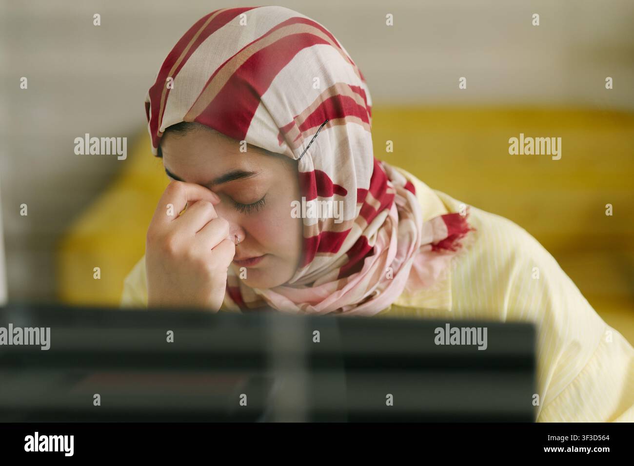 Donna musulmana adulta che sperimenta affaticamento oculare durante il lavoro Foto Stock