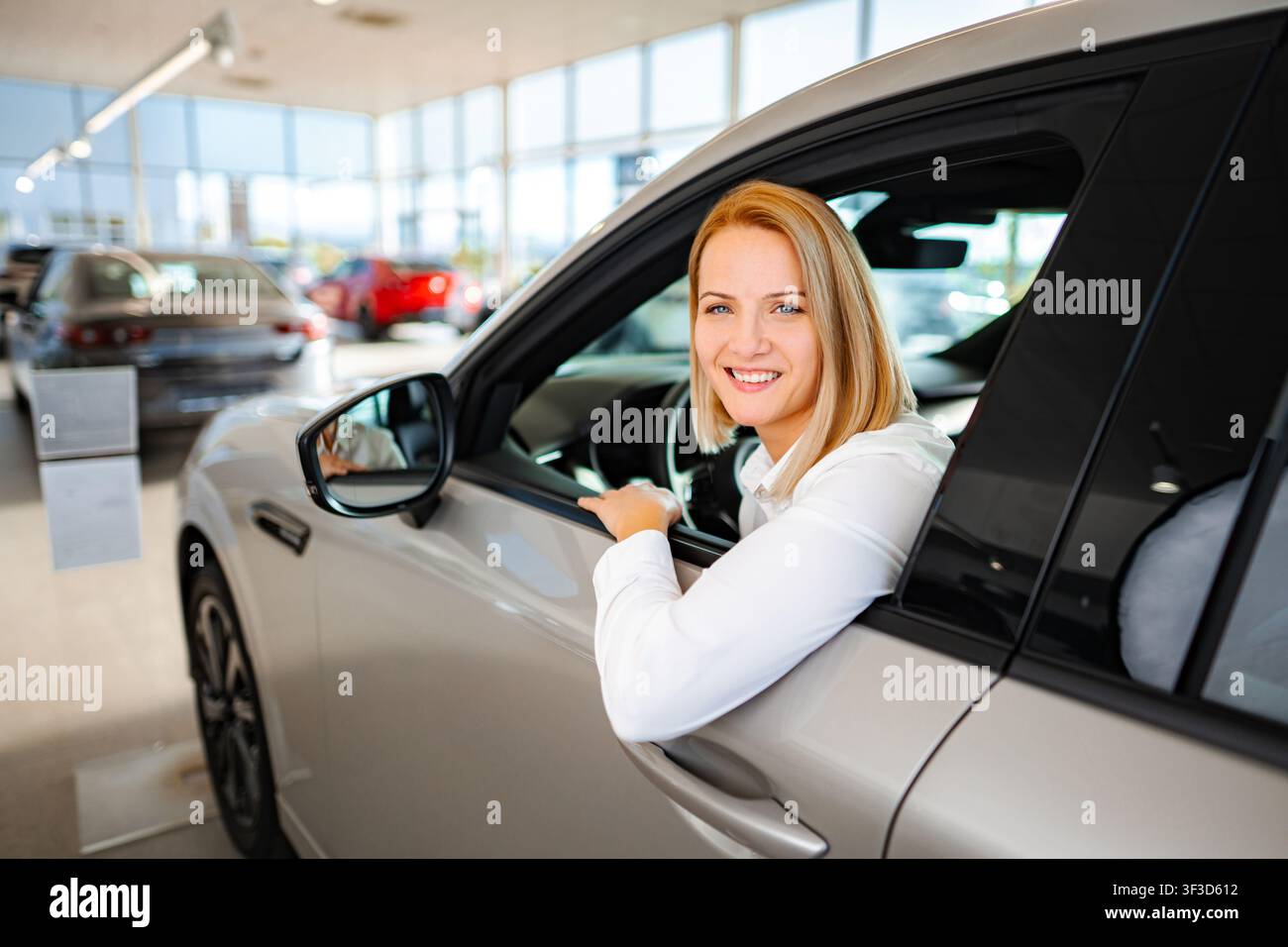 Donna seduta in una nuova auto presso un concessionario, che prende una decisione di acquisto Foto Stock