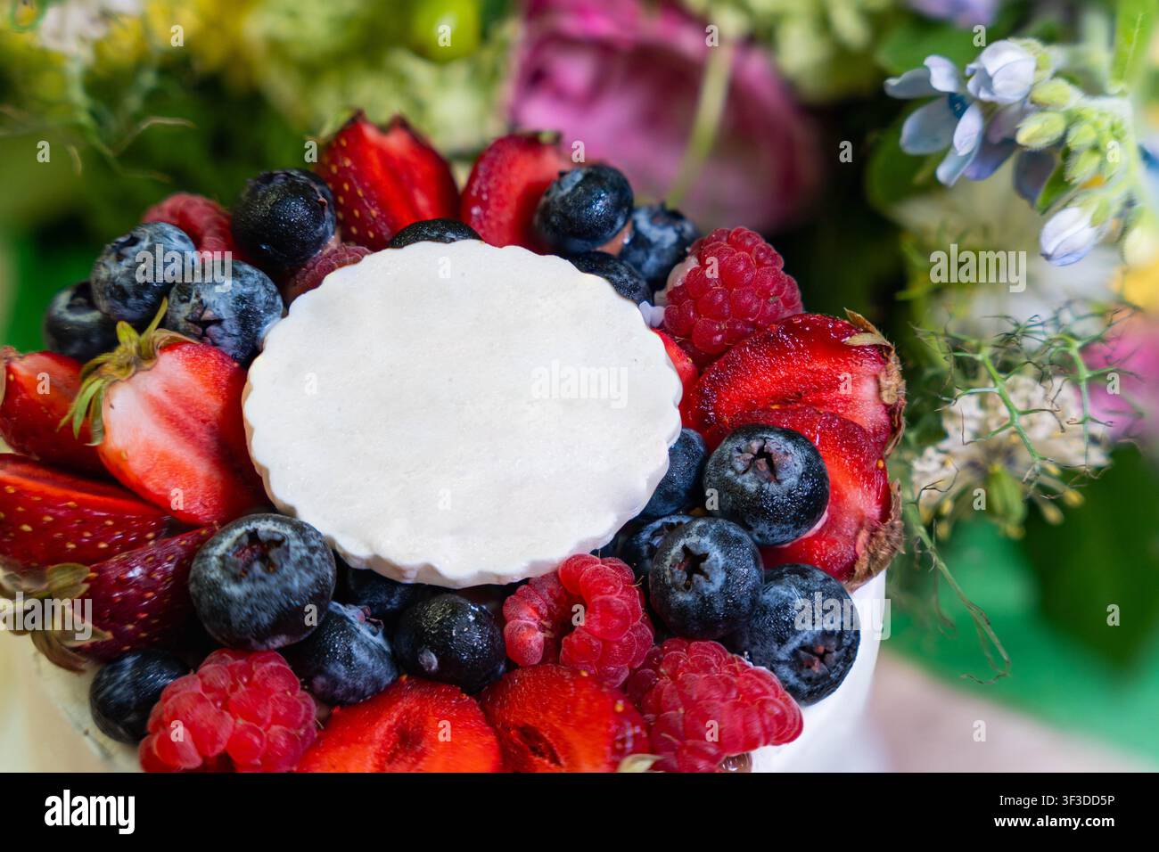 Dessert luminoso alle bacche con fragole, mirtilli e lamponi che circondano un centro bianco liscio, creando una composizione alimentare fresca e festosa Foto Stock
