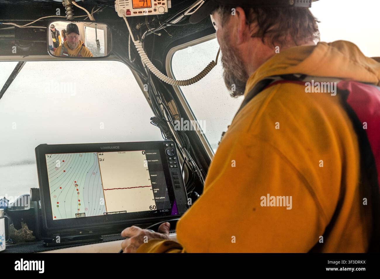 Dale Stewart-Smith nella timoneria del suo peschereccio di aragoste nella baia di St Ann vicino a Englishtown, Nuova Scozia, Canada, sta osservando il tracciatore di carte elettronico con il suo display dell'ecoscandaglio. Nello specchietto retrovisore sopra di lui si vede un secondo membro dell'equipaggio Foto Stock