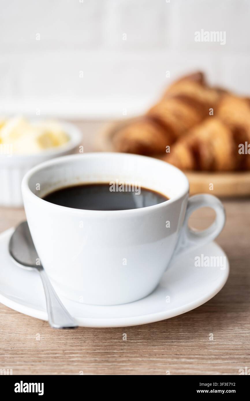 Caffè nero con croissant freschi su tavolo di legno Foto Stock