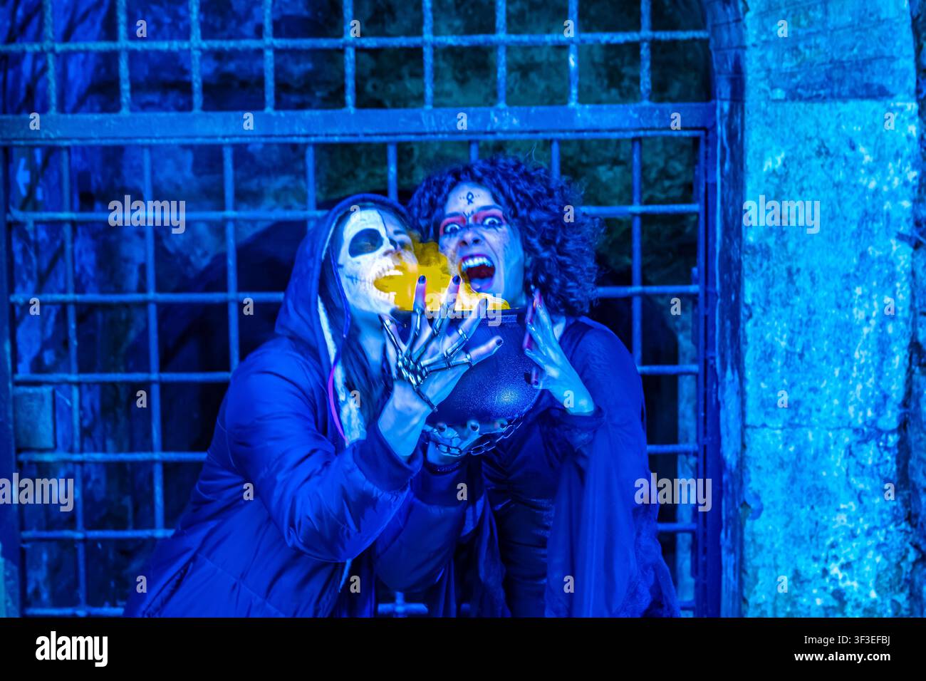 Scheletro e strega di Halloween che lanciano un incantesimo con un calderone luminoso Foto Stock