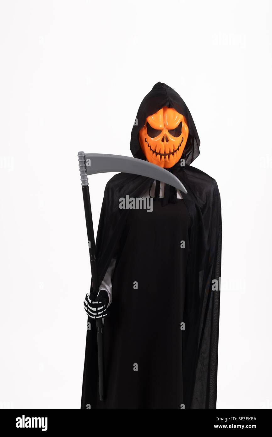 Persona in costume da mietitore di Halloween che tiene una falce in una stanza buia Foto Stock