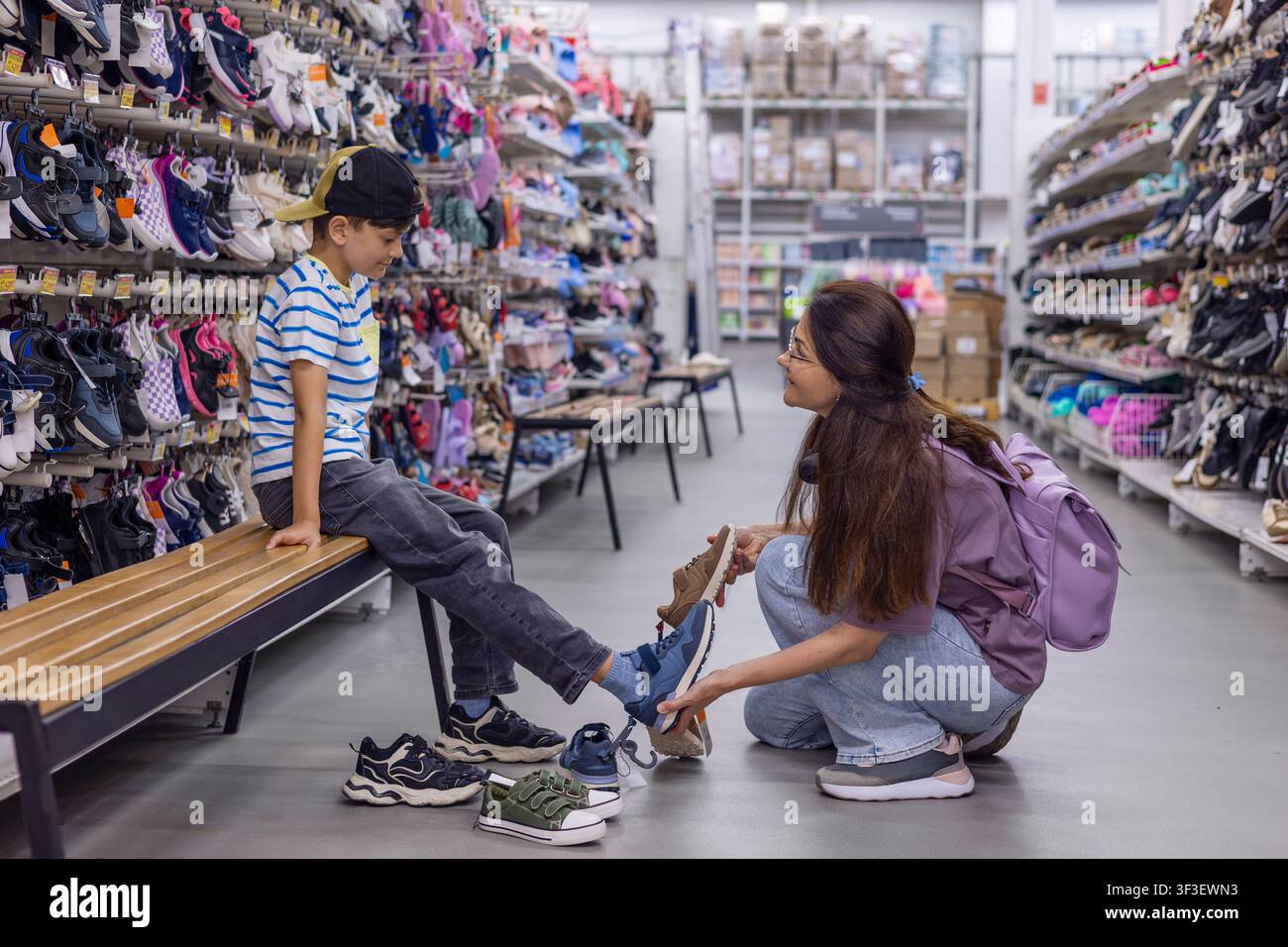 Madre che sceglie nuove scarpe per il figlio in crescita nel negozio di scarpe. Concetto di shopping familiare, crescita dei bambini, preparazione per la scuola e spese intelligenti Foto Stock