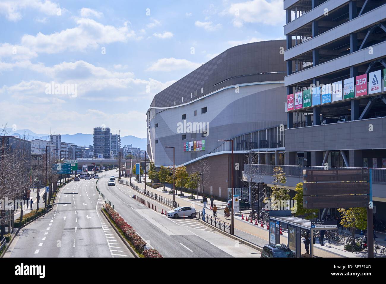 Una scena urbana moderna di strada in Giappone con un grande complesso commerciale contemporaneo con architettura curva distintiva e un adiacente Foto Stock