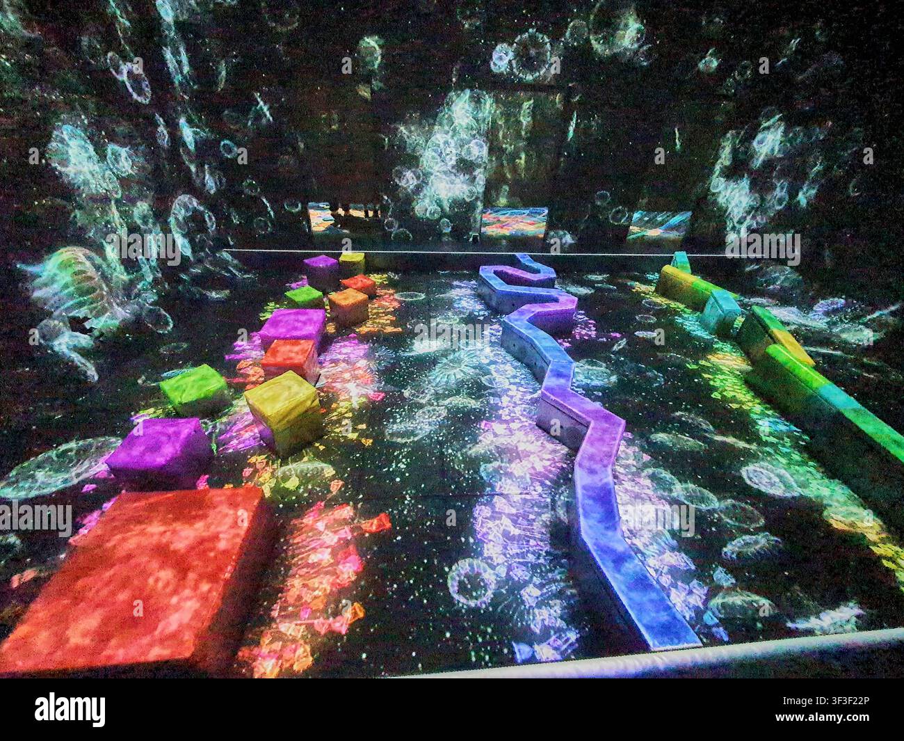 Un'installazione artistica digitale immersiva con blocchi tridimensionali colorati e strutture geometriche curve disposte su una superficie altamente riflettente Foto Stock