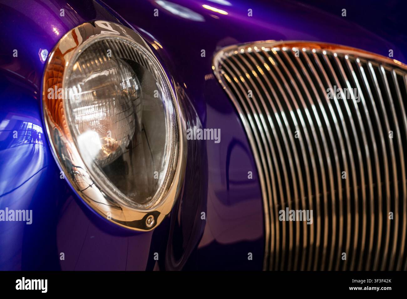 Primo piano dettagliato di un'auto classica viola restaurata che mette in risalto la griglia cromata, il faro e la carrozzeria lucida. Ideale per automotive, restauro, Foto Stock