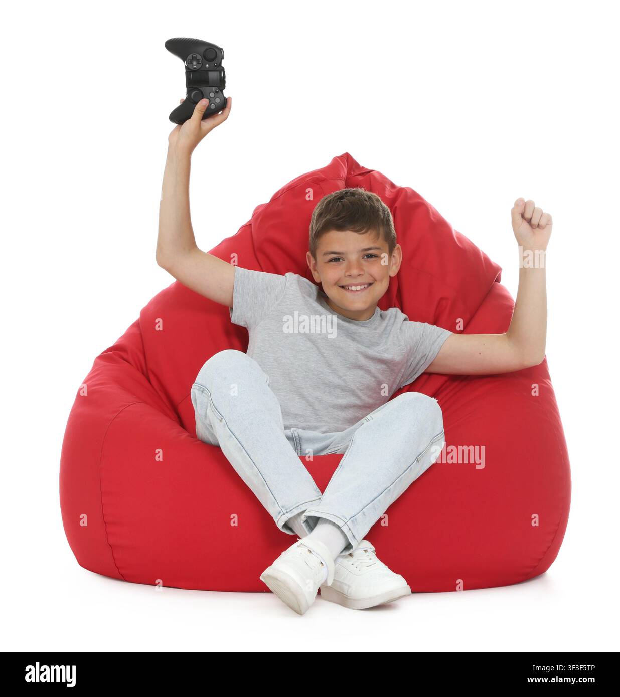 Ragazzo eccitato con controller che gioca a un videogioco su un pouf contro uno sfondo bianco Foto Stock