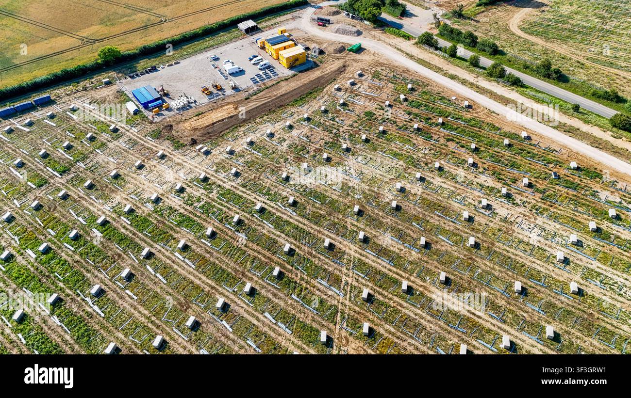 Veduta aerea di un cantiere per la costruzione di una fattoria solare con file di strutture di montaggio metalliche, attrezzature edili e container a Great Wymondley, Engla Foto Stock