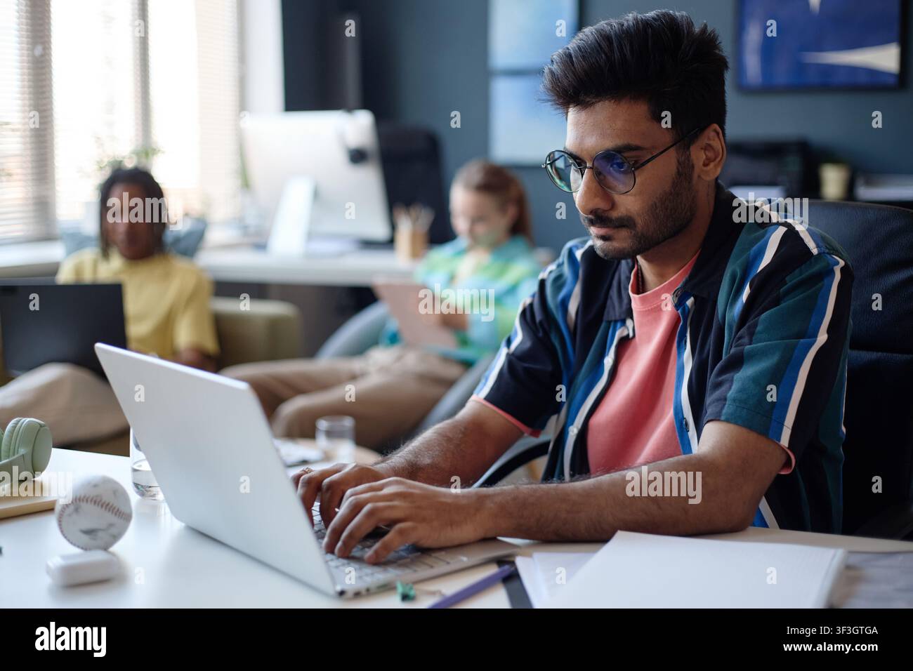 Uomo indiano adulto che lavora su un laptop in uno spazio di ufficio condiviso Foto Stock