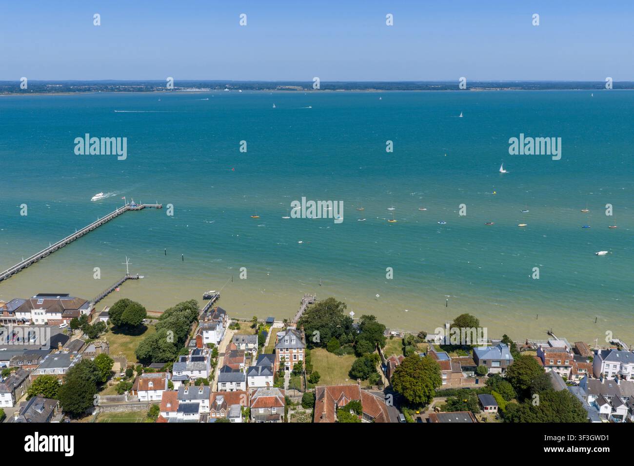 Vista aerea che si affaccia sul Yarmouth Pier e sul Solent sull'Isle of Wight con eleganti case sul lungomare, moli privati, barche a vela e acqua turchese Foto Stock