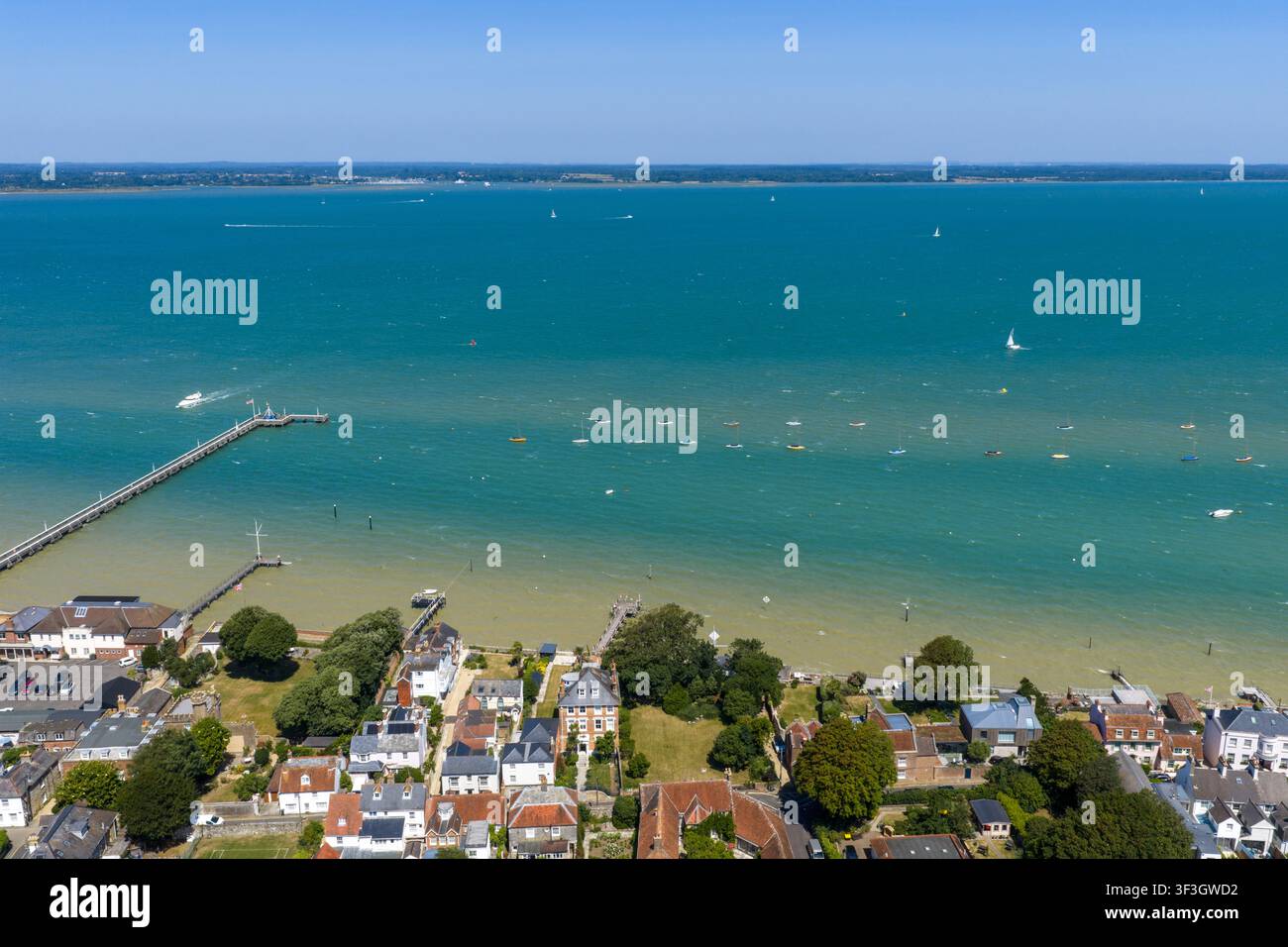 Vista aerea panoramica di Yarmouth Pier e del Solent sull'Isola di Wight che mostra eleganti case sul lungomare, moli privati, barche a vela e l'asta Foto Stock