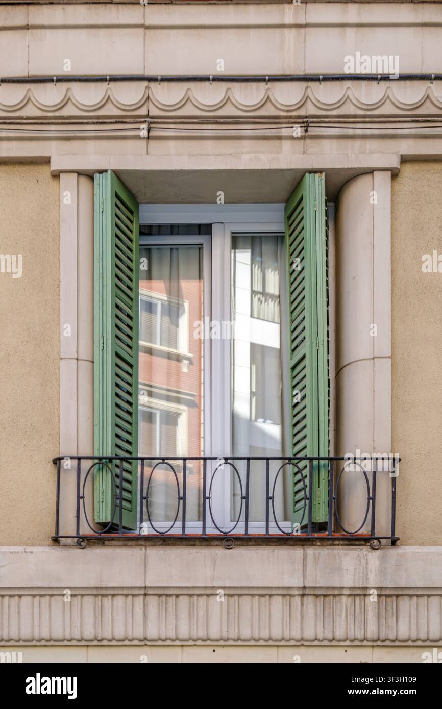 Barcellona – Spagna – 14 luglio 2026: Finestra classica con persiane verdi aperte, balcone in ferro, facciata ornata, riflessione Foto Stock