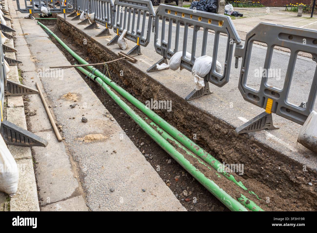 Trincea di servizio con tubi verdi lungo lo scavo stradale Foto Stock