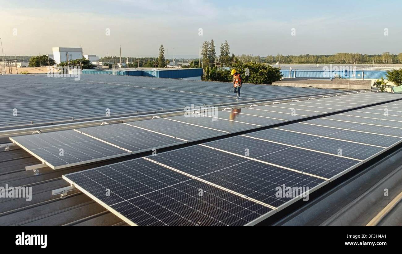 Tecnici che installano binari di montaggio per pannelli solari sul tetto metallico di un edificio industriale come parte di un sistema di energia rinnovabile e di energia solare sul tetto Foto Stock