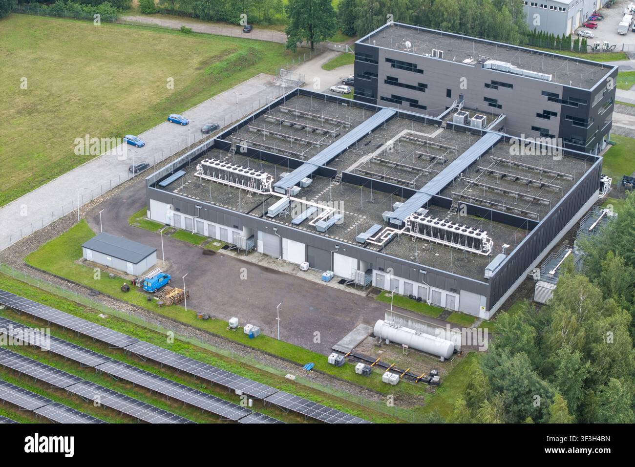 Vista aerea di un moderno edificio per data center con sistemi di raffreddamento HVAC sul tetto, array di pannelli solari adiacenti e aree di parcheggio a Kra Foto Stock