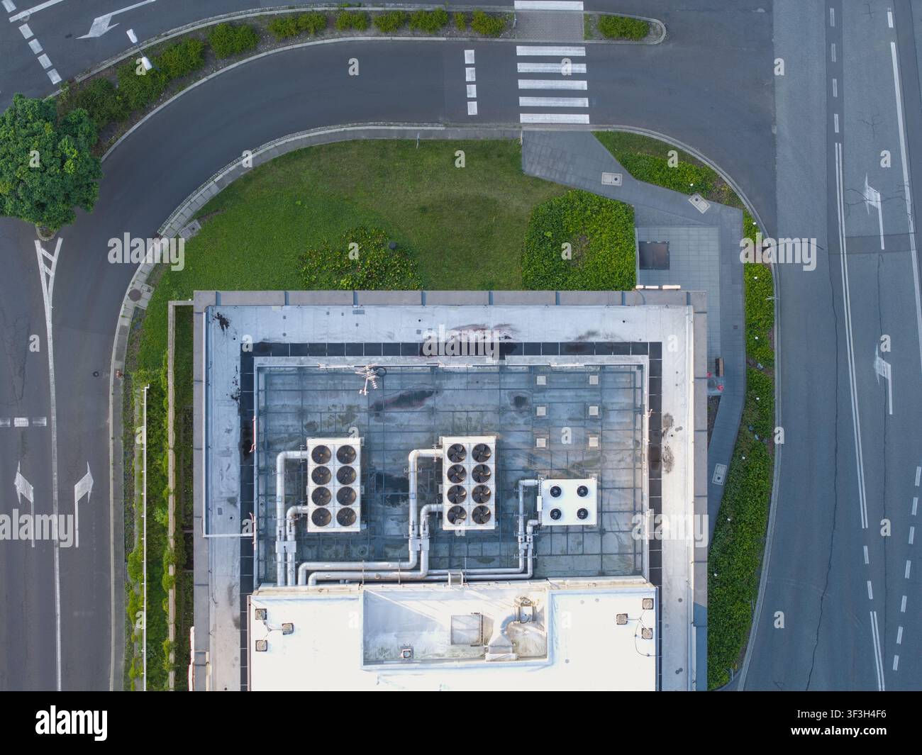 Vista aerea del tetto di un edificio per uffici di un centro dati AI con sistemi di raffreddamento HVAC industriali e tubature metalliche, situato vicino a un incrocio stradale Foto Stock