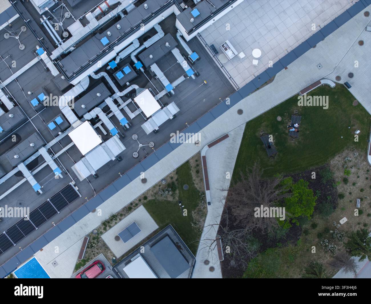 Vista aerea del sistema di raffreddamento HVAC sul tetto di un edificio di un centro dati AI, con spazio verde adiacente e percorsi pedonali lastricati a Cracovia Foto Stock