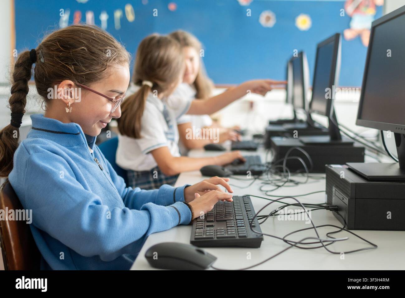 Studente delle elementari che utilizza un computer fisso durante una lezione di tecnologia informatica in un'aula moderna. Foto Stock
