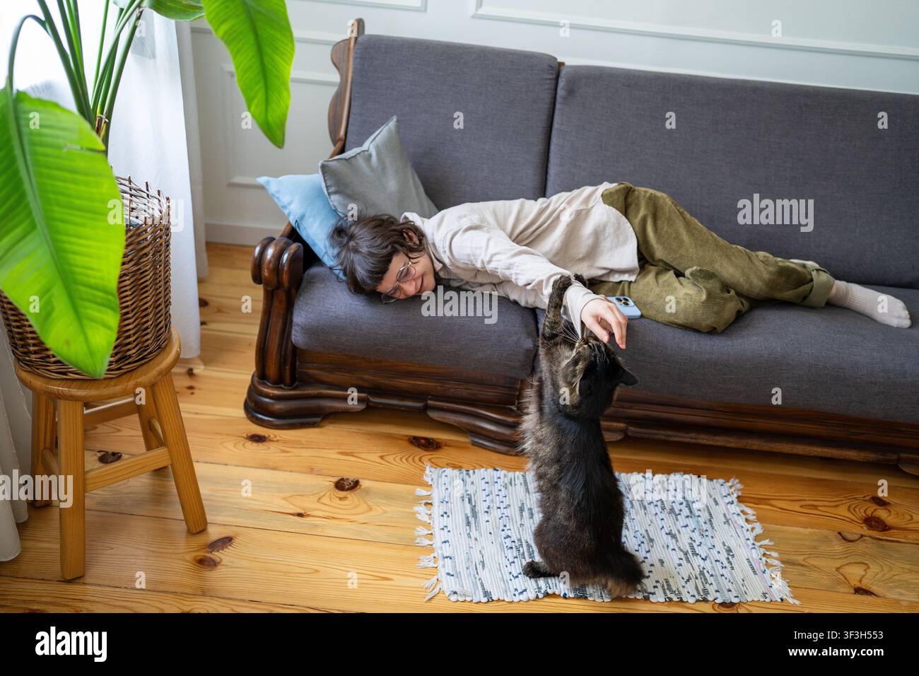 Donna allegra che gioca con il gatto mentre si rilassa completamente sul divano in camera, felicità a casa nel fine settimana. Foto Stock