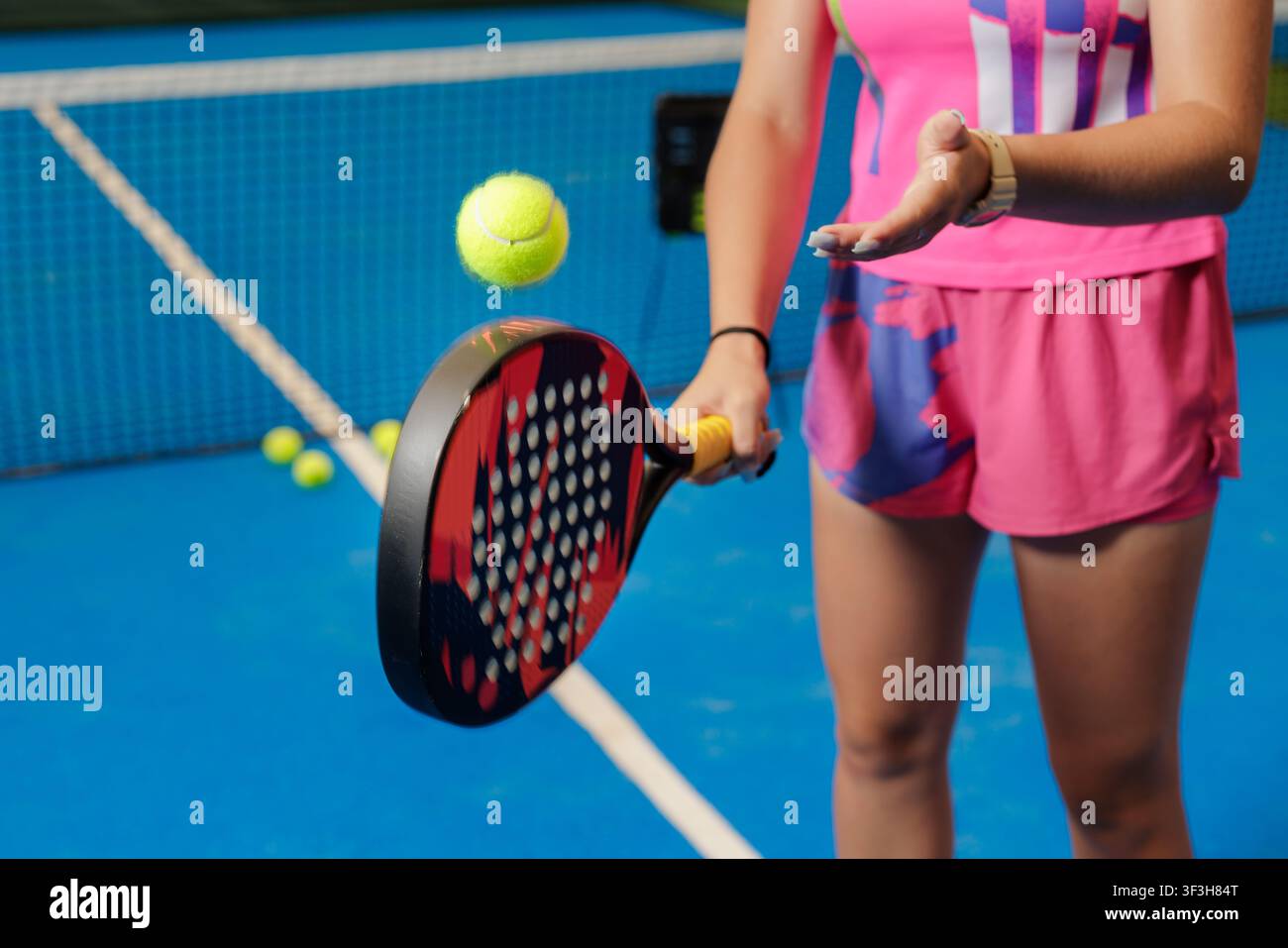 Un allenatore di padel dimostra tecniche di allenamento mentre tiene una racchetta e si prepara a colpire una palla, mostrando l'ambiente di allenamento dello sport. Foto Stock