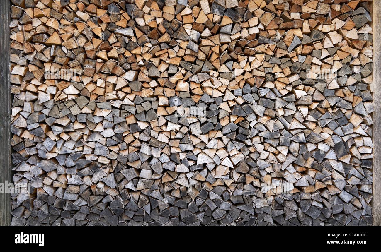 Legna da ardere impilata in varie tonalità tra due pali di legno Foto Stock