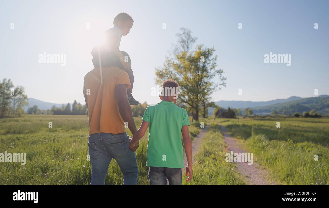 Padre e due figli camminano insieme su un sentiero nel campo al tramonto. Creano ricordi e rafforzano il loro legame all'aperto nella natura. Foto Stock