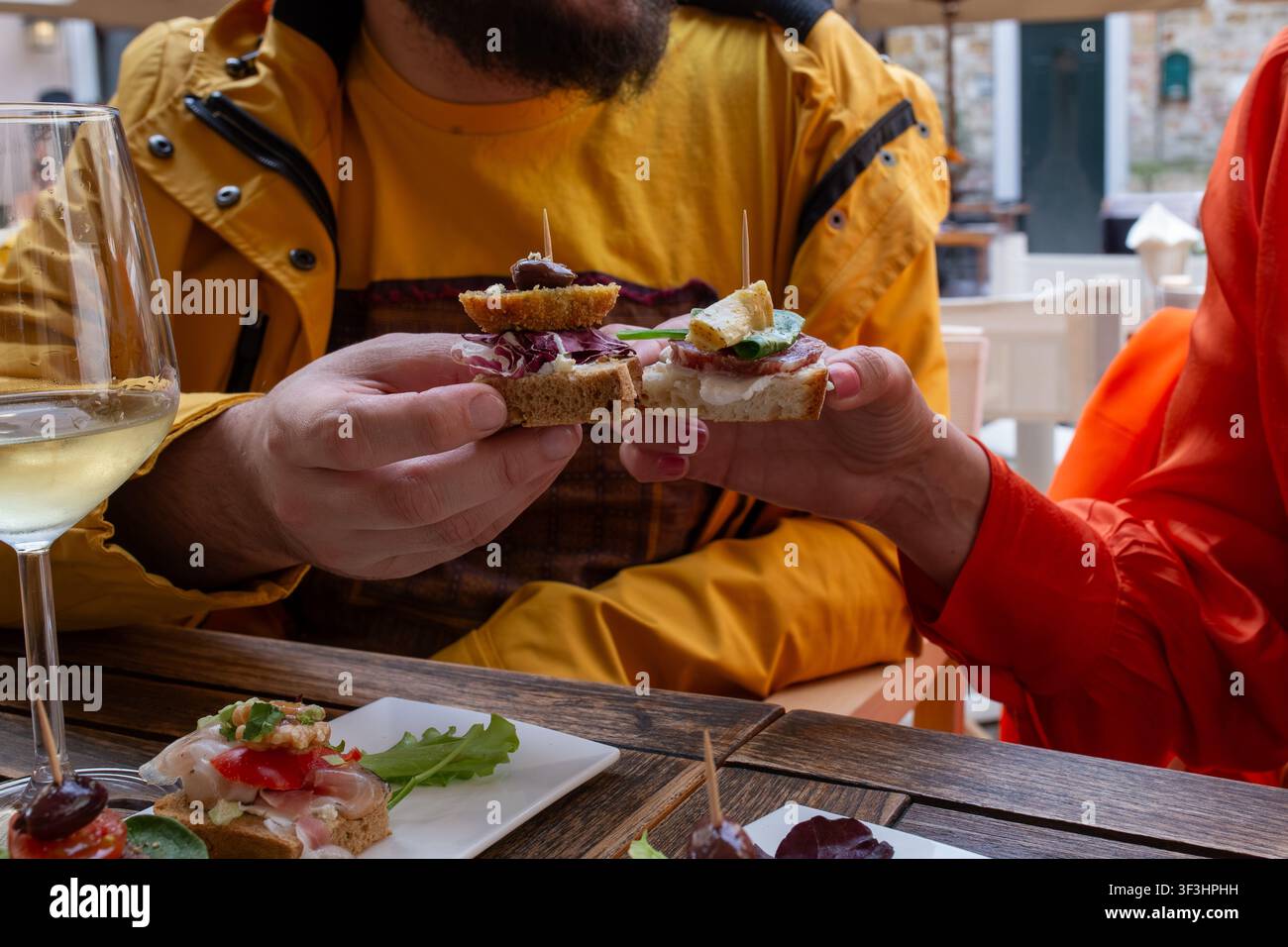 Due persone che brindano con cicchetti su pane tostato, condividendo un aperitivo informale. Il gesto di scambiare crostini tra amici evoca i convivi Foto Stock
