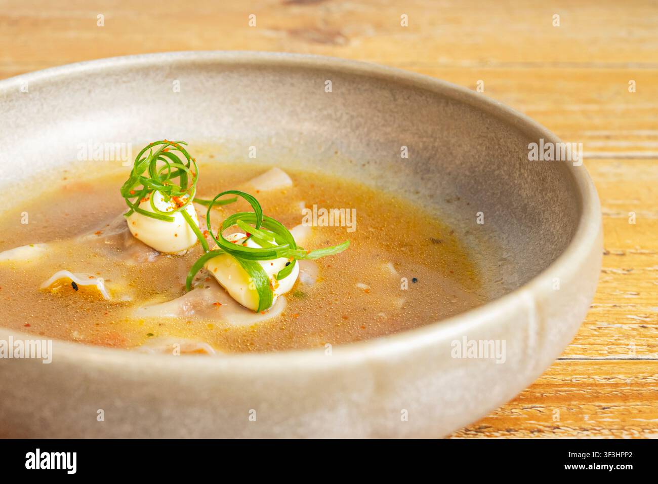 Gnocchi wonton in brodo dorato saporito, guarniti con nastri di scalogno arricciati, fiocchi di peperoncino e condimento a base di panna in una ciotola di ceramica. Foto Stock