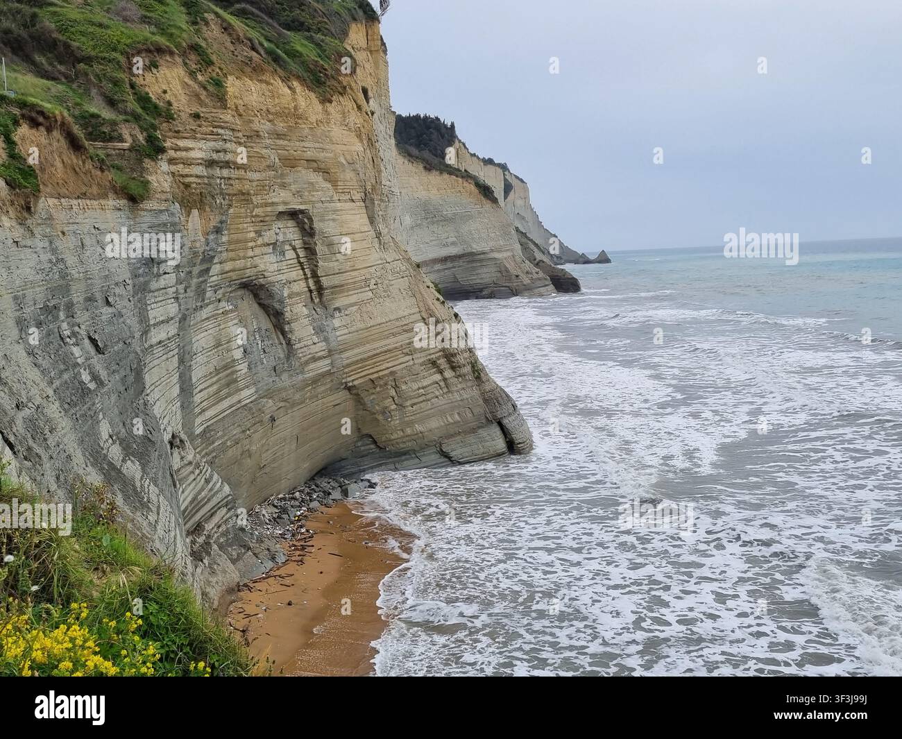 Scogliere di argilla bianca stratificate della spiaggia di Loggas a Peroulades che cadono nel mare Ionio tempestoso sotto un cielo grigio, costa nord-occidentale dell'isola di Corfù, Grecia - Immagine stock catturata con smartphone