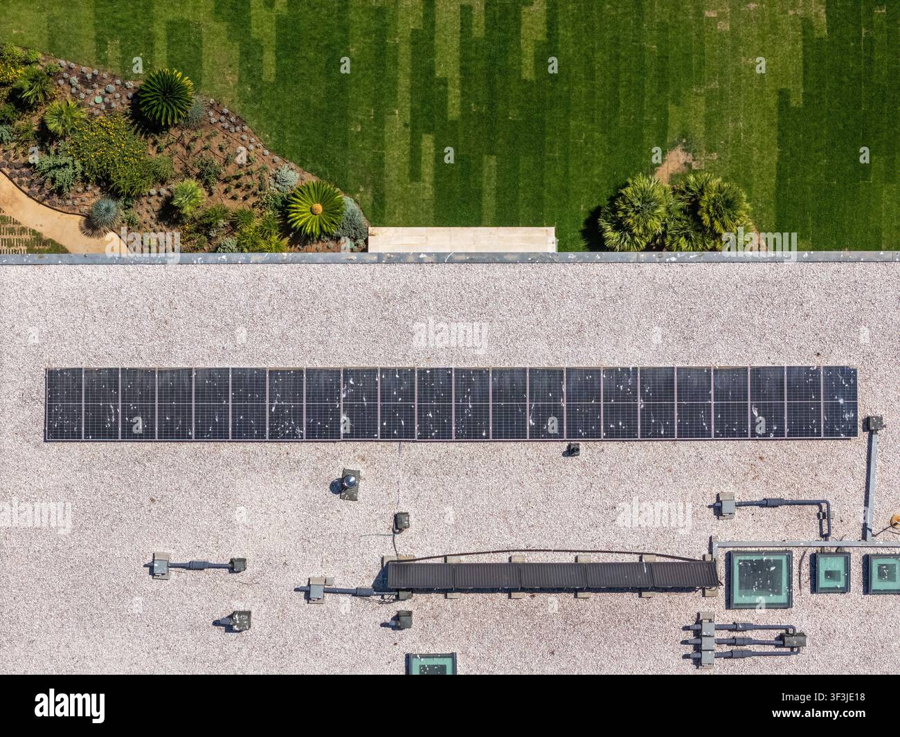 Vista aerea di una fila di pannelli solari installati su un tetto piatto con prato verde adiacente e area giardino a Cascais, Lisboa, Portogallo. Foto Stock