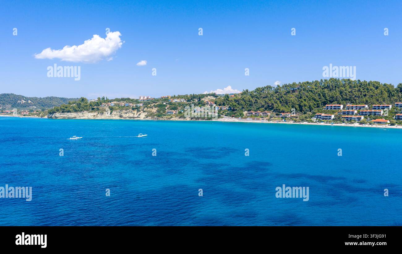 Spiaggia di Possidi, Grecia 11 luglio 2026. Vista aerea luminosa e soleggiata della spiaggia di Possidi che mostra un mare turchese, due barche, una riva sabbiosa e colline boschive con s Foto Stock