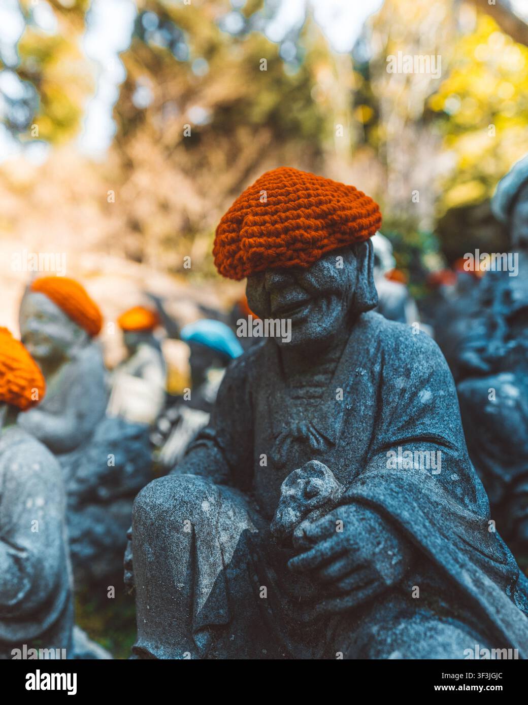 Vista di statue Jizo in pietra che indossano cappelli di maglia arancione brillante in un ambiente esterno sereno in Giappone. Foto Stock