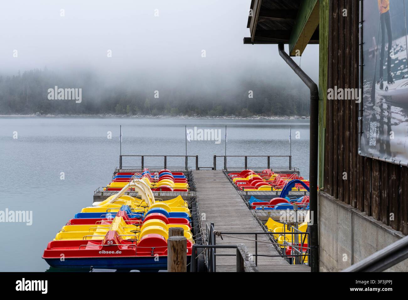 Garmisch-Partenkirchen Germania – 23 settembre 2025: Barche a remi ormeggiate sul lago Eibsee con la nebbia che avvolge la foresta vicina in Germania Foto Stock