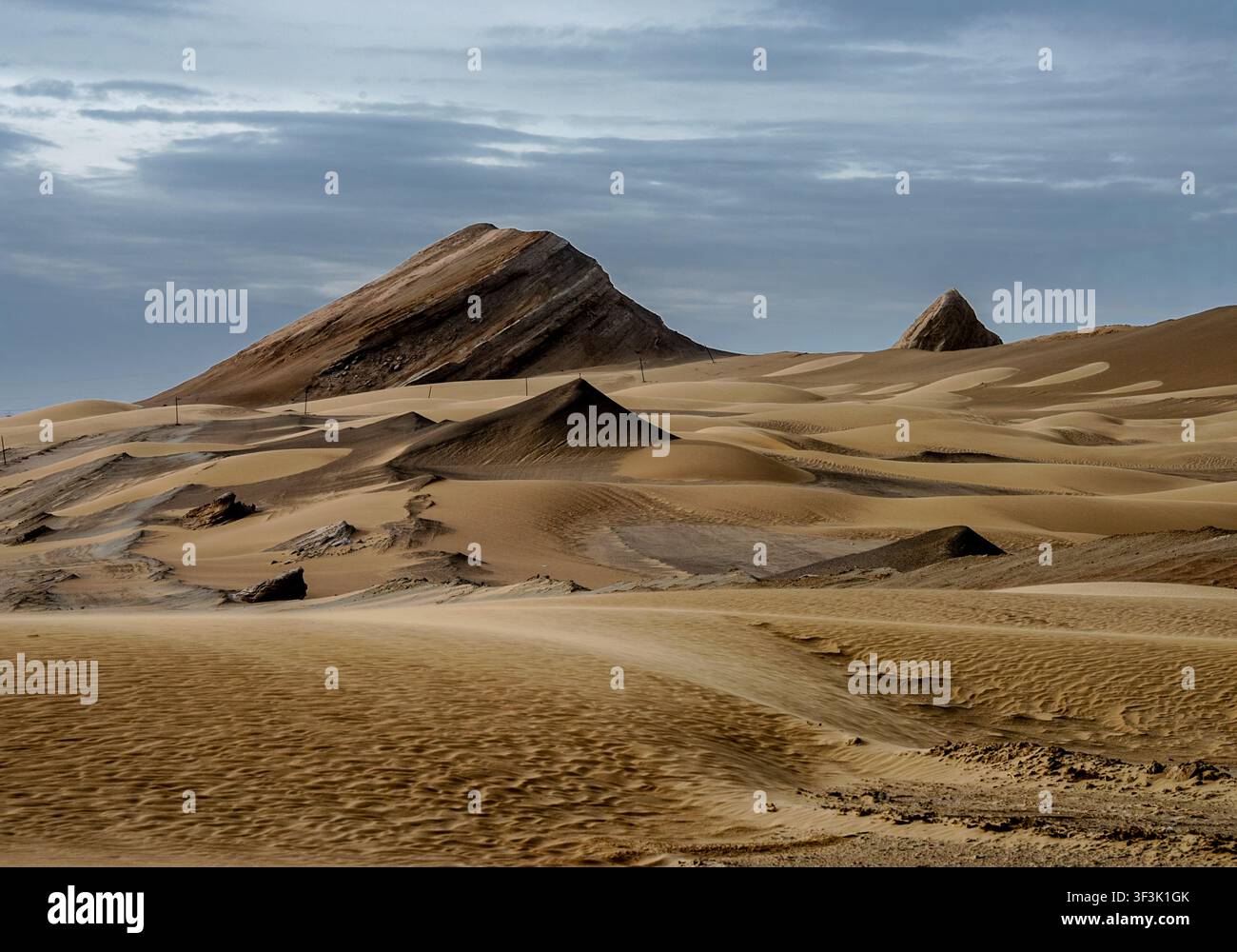 Le drammatiche dune cantanti di Mingsha Shan vicino a Dunhuang presentano dune di sabbia modellate dal vento che circondano picchi rocciosi scuri e frastagliati sotto un cielo cupo in C Foto Stock